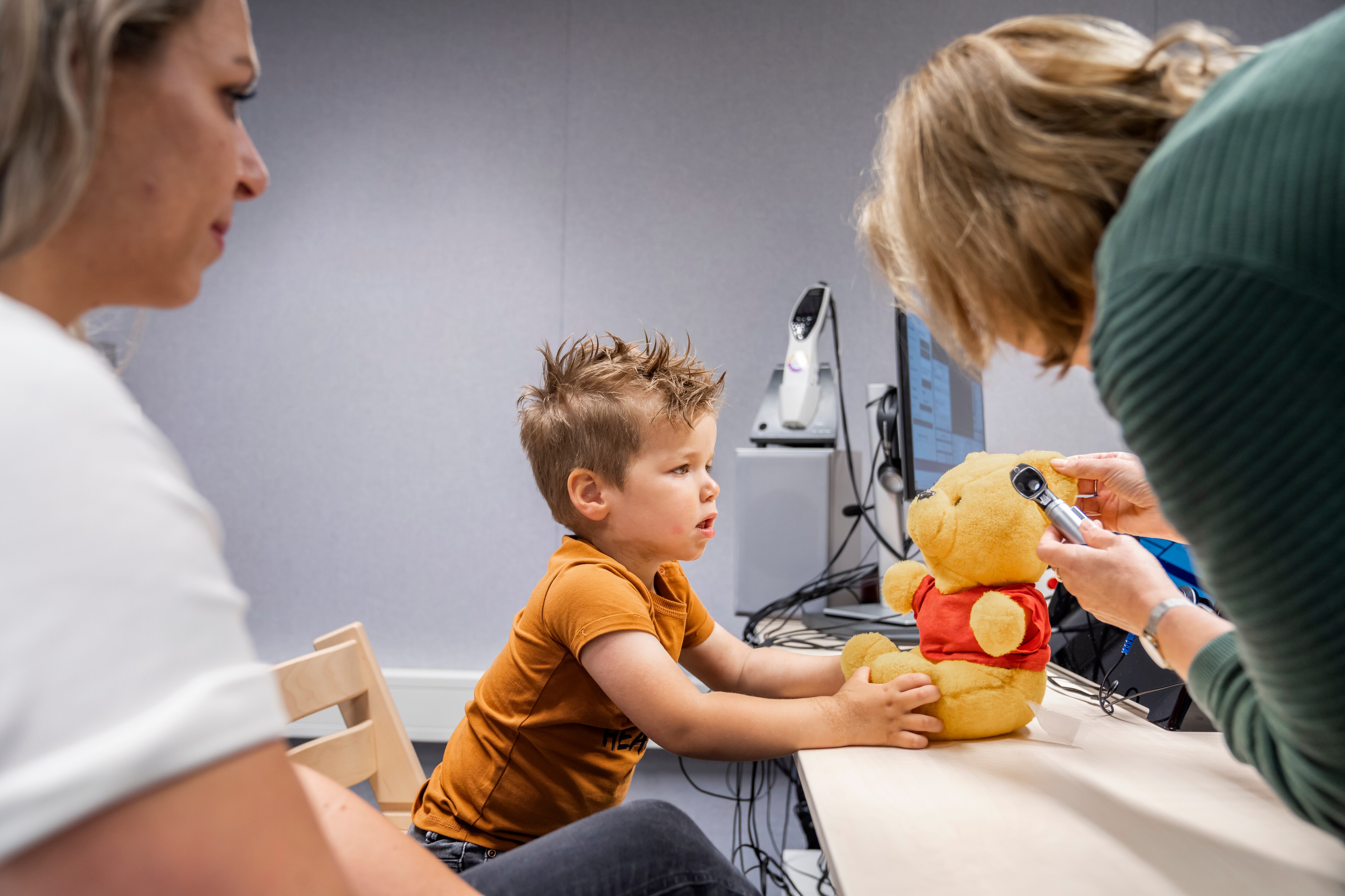Audioloog doet op teddybeer van een jongen voor hoe ze in het oor kijkt