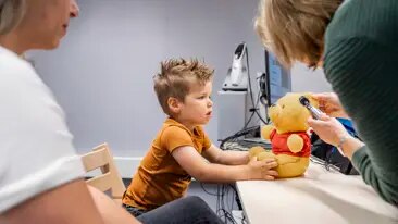 Onderzoek op een speelse manier Audioloog doet op teddybeer van een jongen voor hoe ze in het oor kijkt